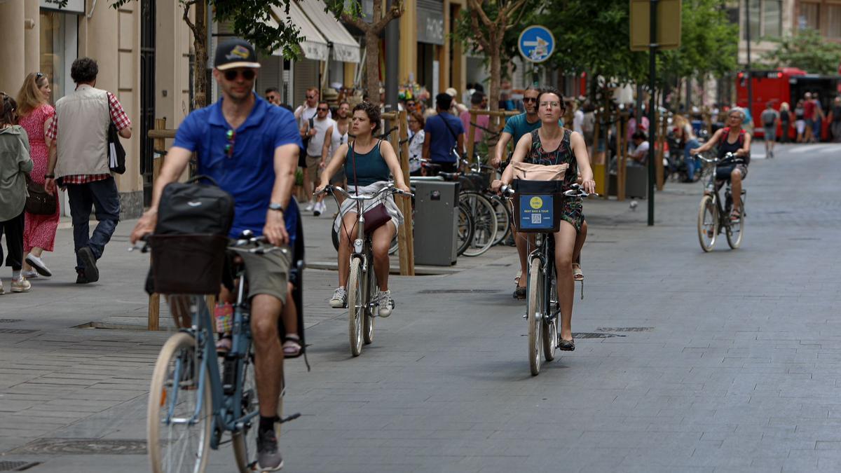 Algunos turistas con bicis de alquiler pasean por el centro de València