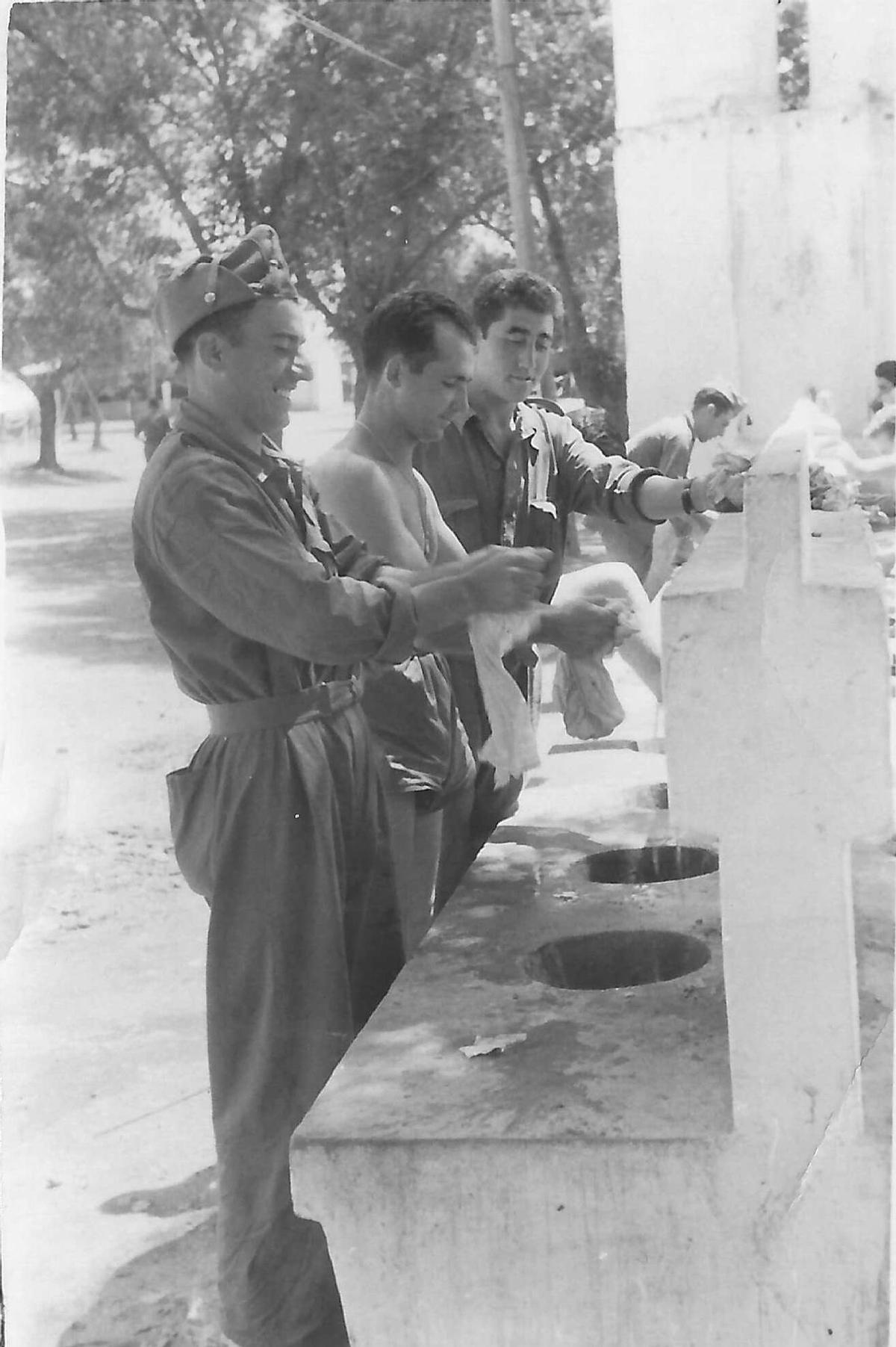 Emilio García junto a otros compañeros en la fuente lavando su ropa.
