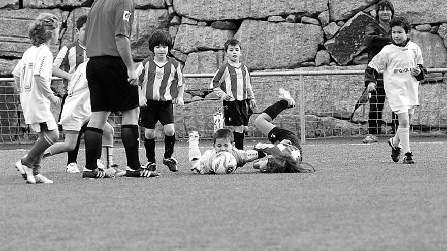 Dos pequeños caen sobre el césped al disputar el balón