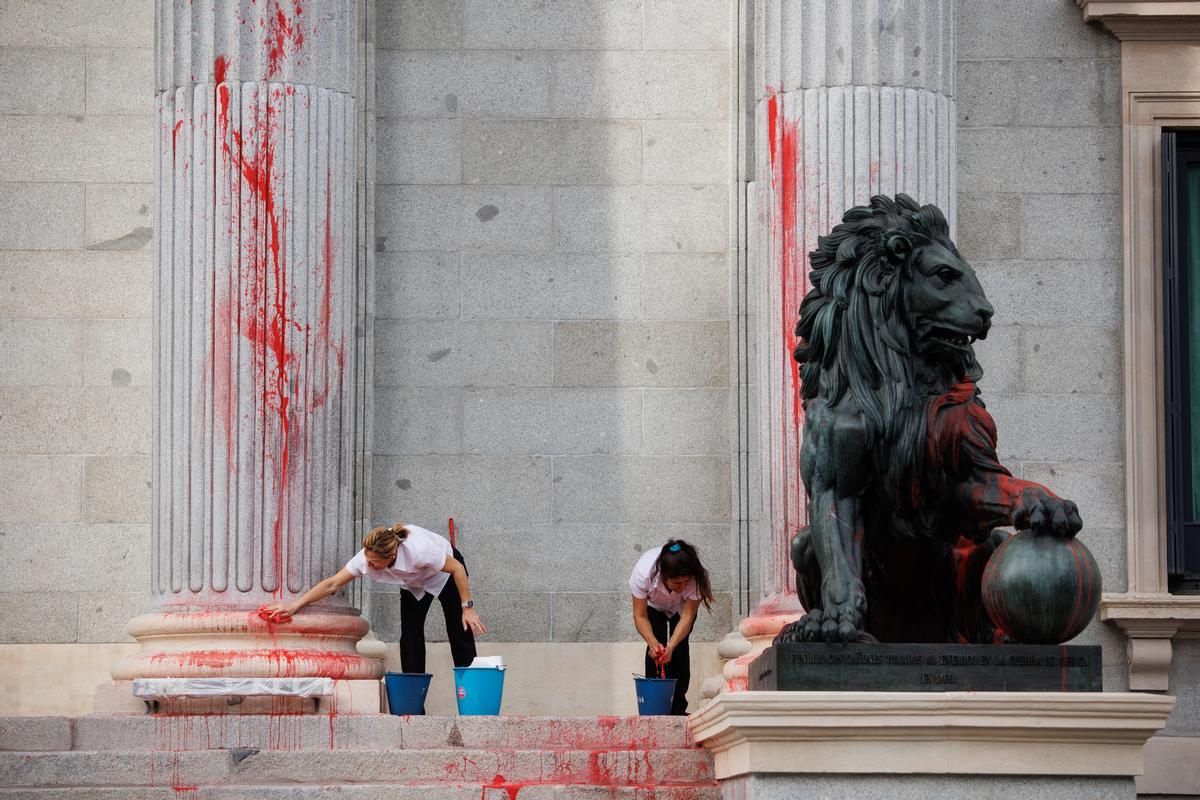 Dos operarias limpian el león del Congreso tras ser pintado en una protesta de Futuro Vegetal y Rebelión Científica.