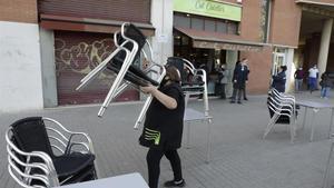 Una mujer recoge las siillas de la terraza de un bar de Poblenou.