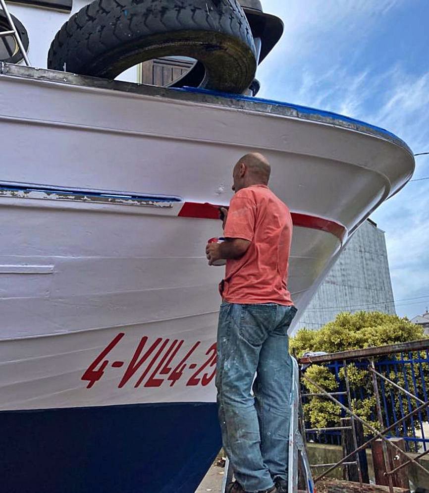 Un hombre pinta el casco de un barco auxiliar de acuicultura.