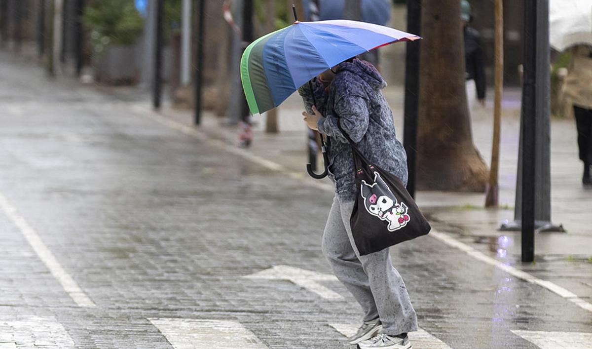 Una persona se resguarda con un paraguas de la lluvia y el viento en Huelva.
