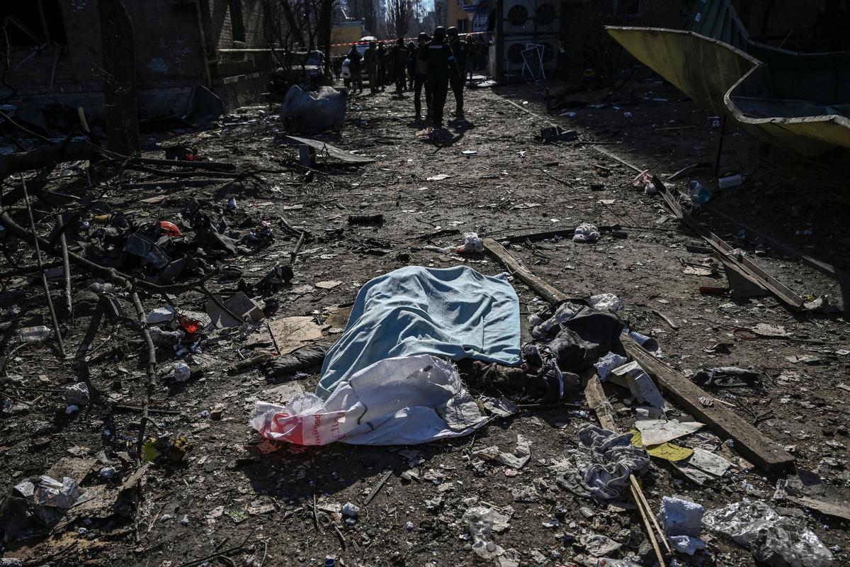 Un cuerpo cubierto con una manta yace entre los daños en una zona residencial después de un bombardeo en Kiev el 18 de marzo de 2022, mientras las tropas rusas intentan rodear la capital ucraniana como parte de su lenta ofensiva
