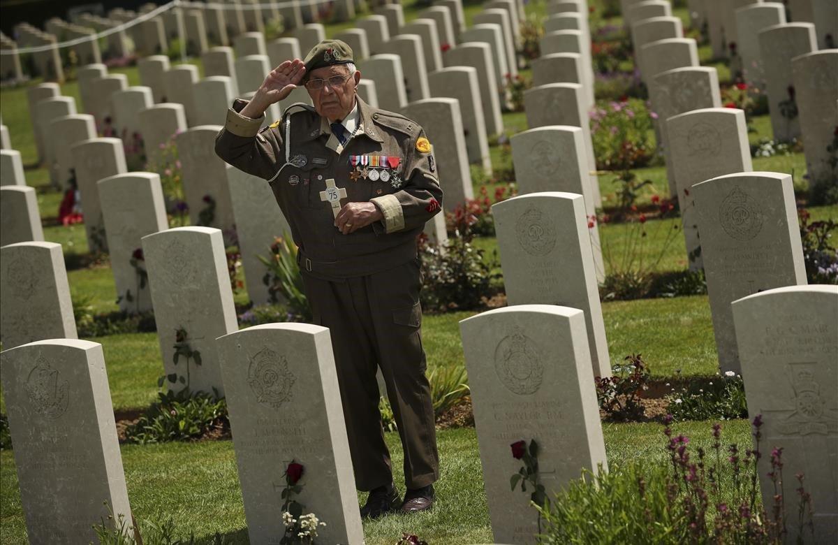 Un veterano de la Segunda Guerra Mundial saluda mientras posa en el cementerio de la guerra de Bayeux, Normandía, Francia.