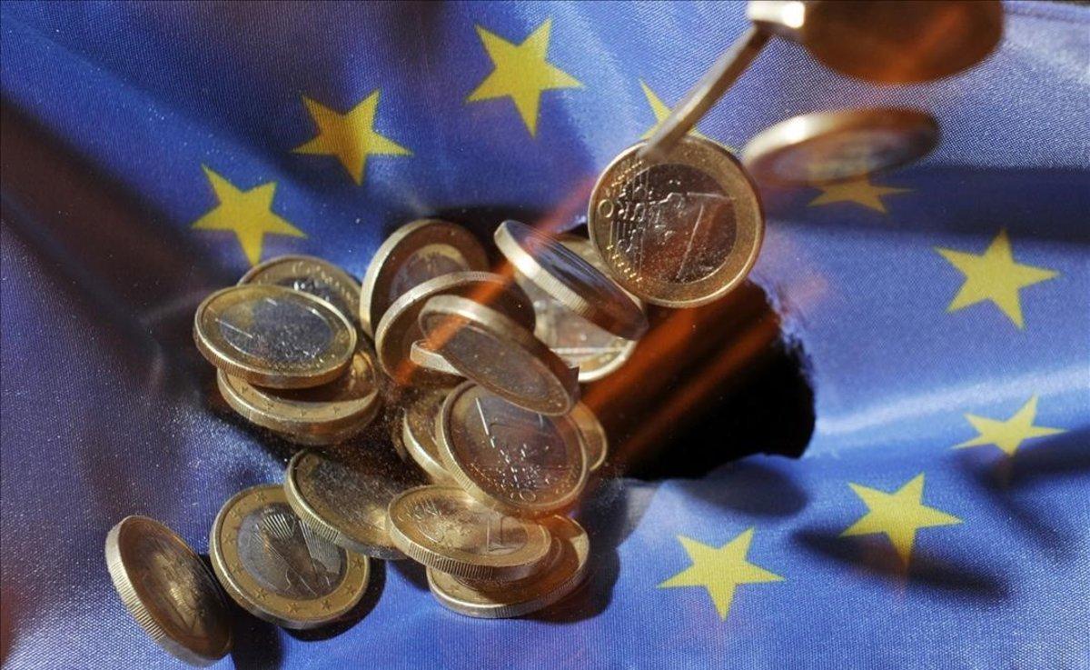 Un puñado de monedas de euro sobre la bandera de la Unión Europea.