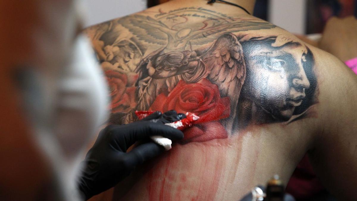 Un profesional de un estblecimiento del sector realiza un tatuaje en la espalda de uno de sus clientes.