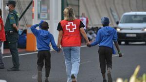 Un efectivo de la Cruz Roja escolta a dos de los menores migrantes.
