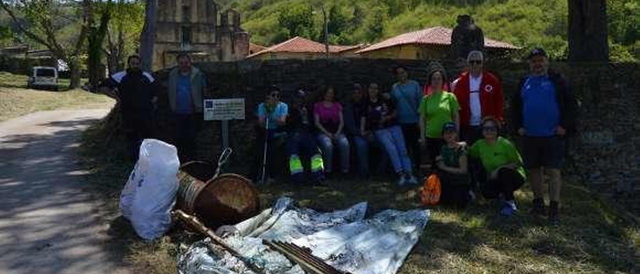 Voluntarios, con la basura que recogieron en el tramo Tineo-Obona. Al fondo, el monasterio.