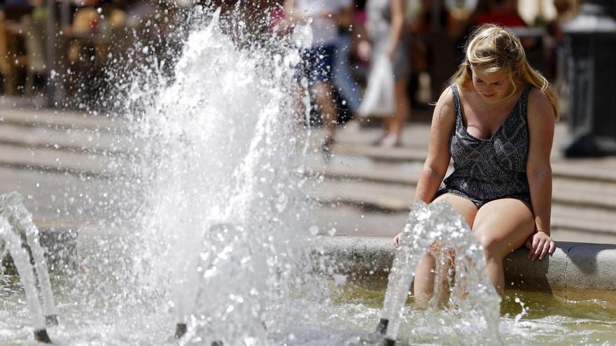 Una turista se refresca en la fuente de la plaza de la Virgen.