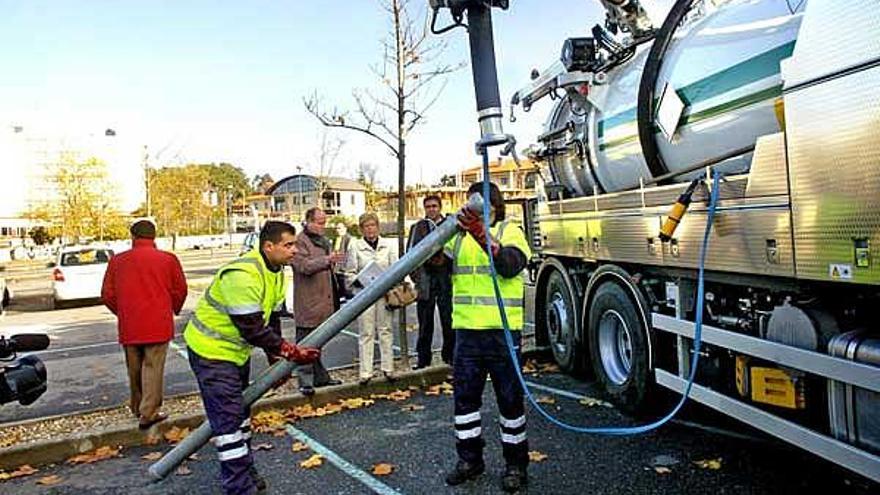 Dos operarios manejan el brazo del camión ante Abelairas y responsables de Aqualia