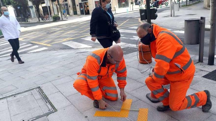 Dos operarios señalizan una acera de sentido único en Santiago.