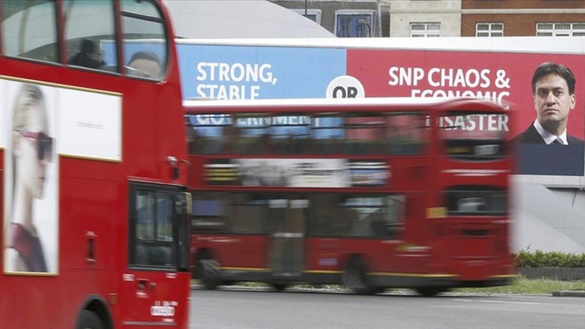 Dos autobuses pasan junto a una valla publicitaria de Cameron y Miliband, en Londres, este miércoles.