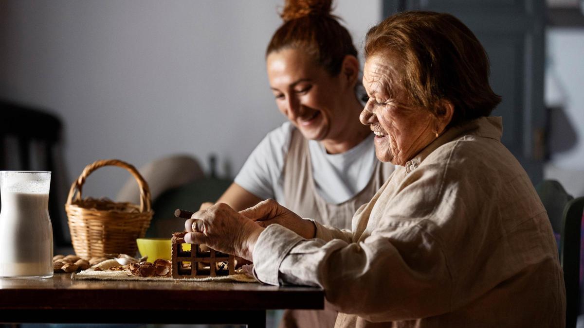 Una profesional de ayuda a domicilio, ayuda a una usuaria del servicio a abrir unas nueces.