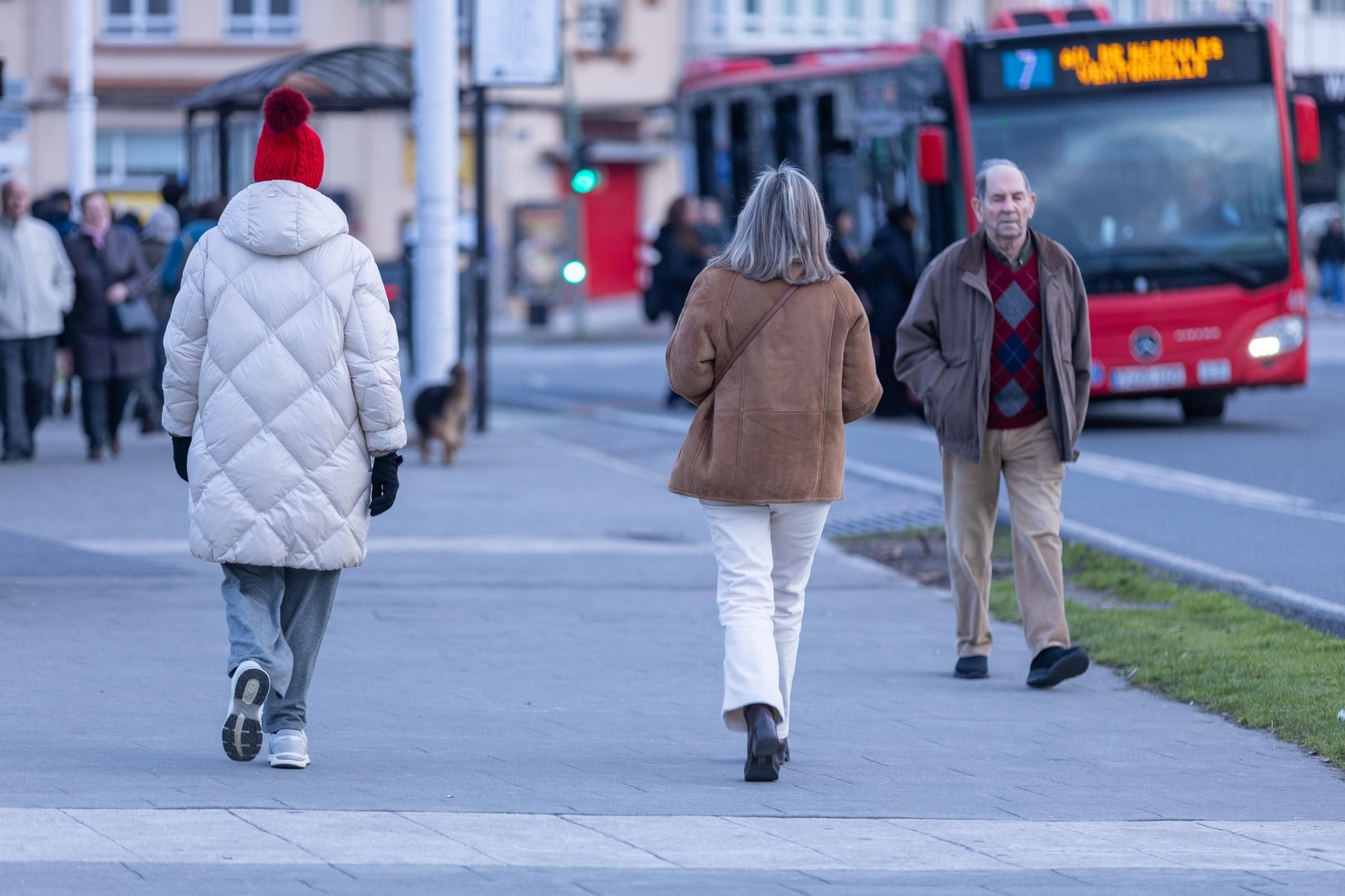 Viandantes caminan por el paseo marítimo de A Coruña con abrigos, gorro y guantes.