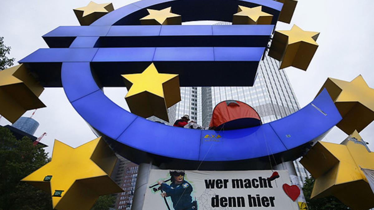 A demonstrator sits in the euro sculpture as the waits for police to clear the camp of occupy protestors in front of the European Central Bank (ECB) in Frankfurt