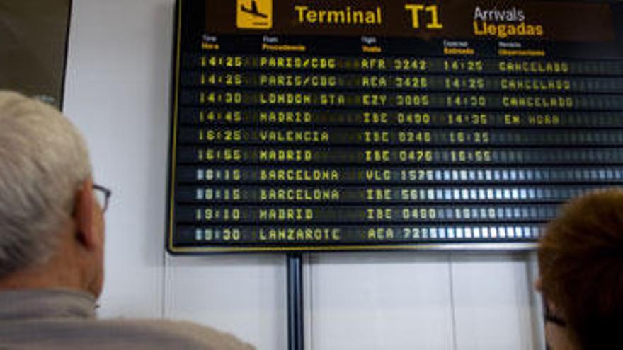 Pasajeros en el aeropuerto de Asturias observando los paneles informativos.