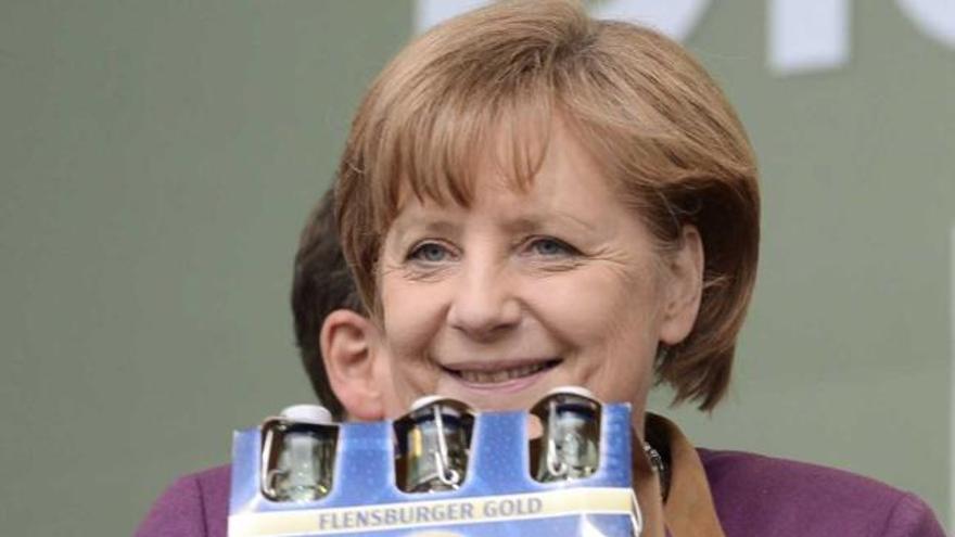 Angela Merkel sostiene una caja con cervezas durante un acto de su partido.