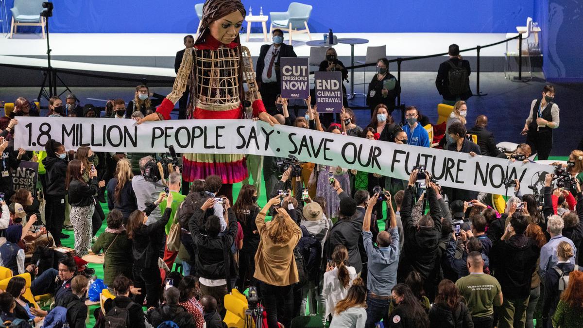Participantes en la cumbre COP26 de Glasgow, con una pancarta reivindicativa, junto a la marioneta gigante Little Amal.