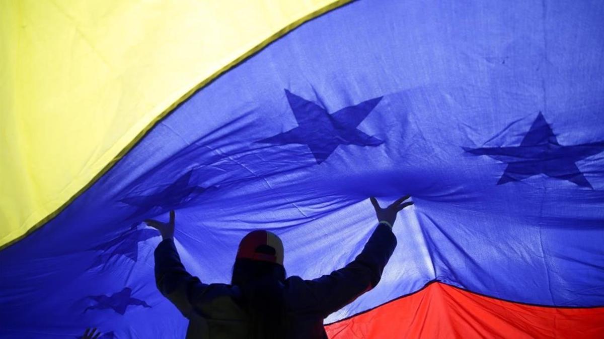 Una mujer sujeta una gran bandera de Venezuela en las manifestaciones en la Puerta del Sol en Madrid