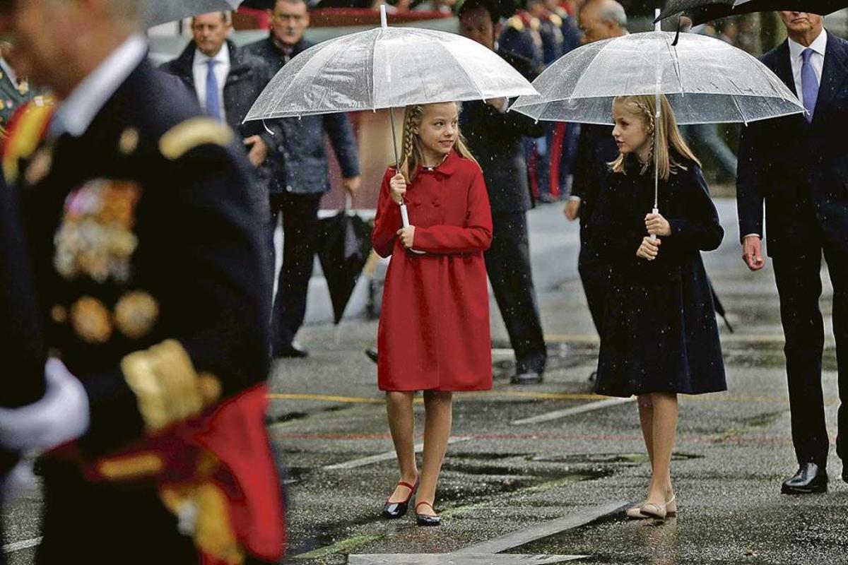 La Princesa de Asturias, Leonor de Borbón, a la derecha, y su hermana Sofía, protegiéndose de la lluvia con los paraguas en el desfile de la Fiesta Nacional el año pasado.