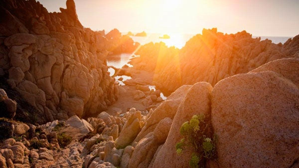 El sol brilla a través de la rocas en una playa de Cerdeña