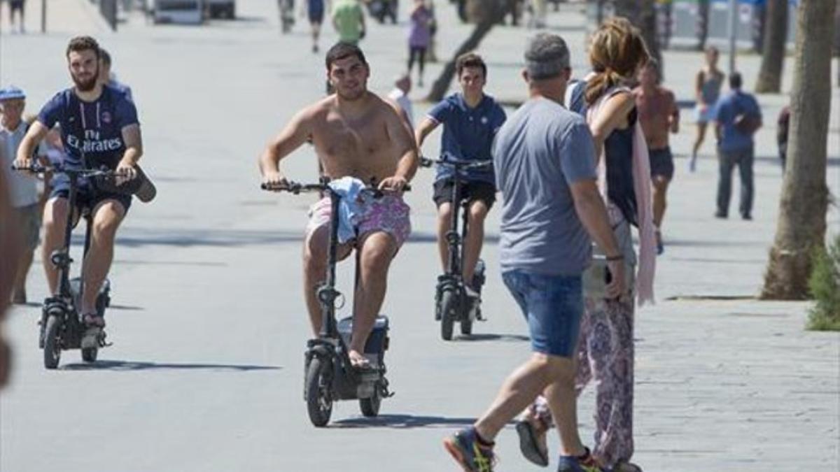 Tres usuarios de patinete eléctrico, en el paseo marítimo de la Barceloneta.
