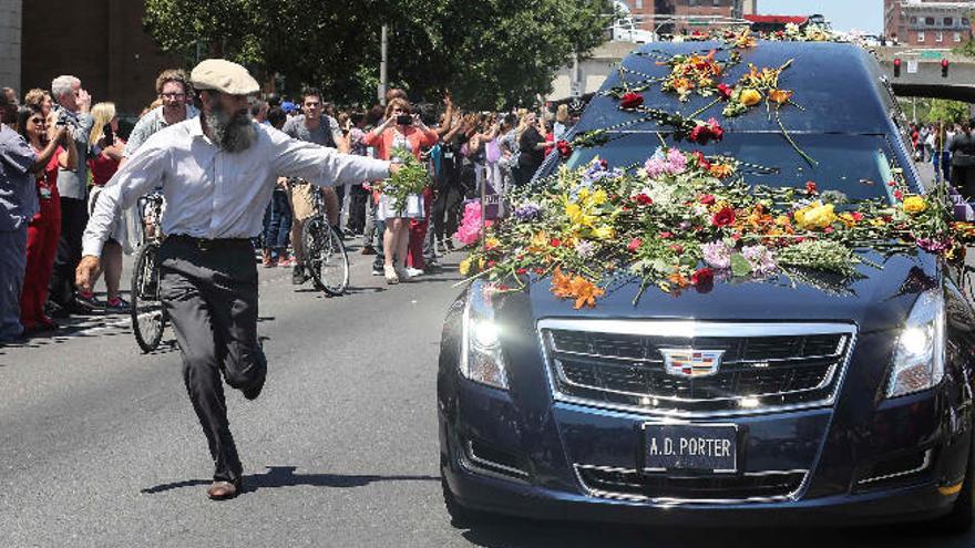 Un hombre corre para dejar flores sobre el coche fúnebre.