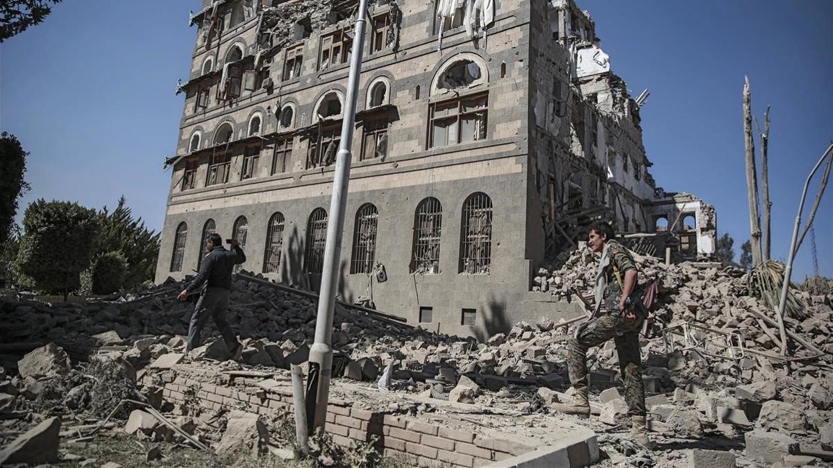 Dos rebeldes yemeníes inspeccionan las ruinas de edificios destruidos por los bombardeos en Saná