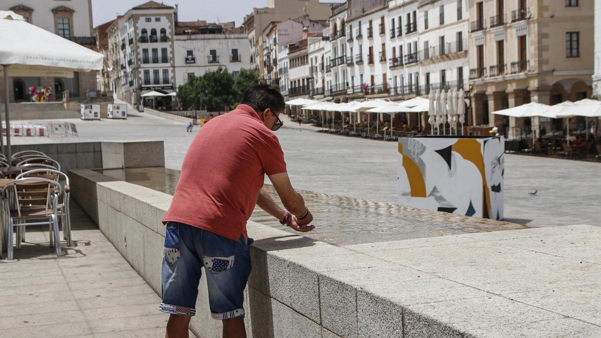 Un viandante se refresca en una de las fuentes de la plaza Mayor de Cáeres.