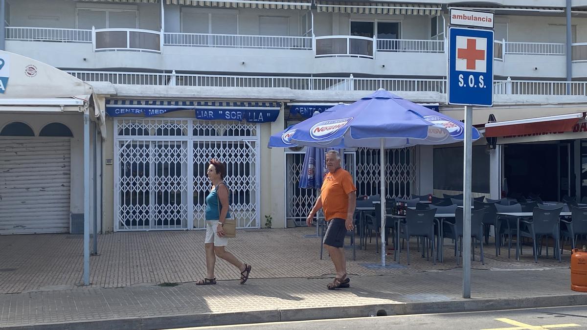Dos personas pasean por delante del consultorio auxiliar de Sorolla, cerrado en Peñíscola desde el año 2020.