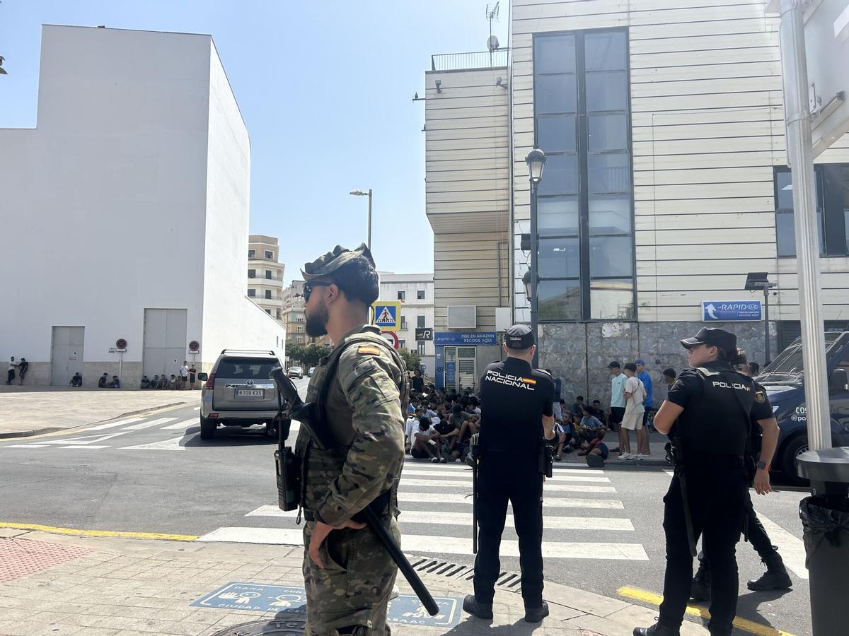 Varios militares dan apoyo a efectivos de la Policía Nacional al lado de una comisaría en la que un grupo de menores espera para ser filiado, a 10 de agosto de 2026, en Ceuta (España). La ciudad acoge a miles de personas pendientes de retorno, entre ellas más de 1.300 menores, mientras las convocatorias difundidas en redes sociales hacen temer una nueva entrada masiva de migrantes. 10 AGOSTO 2026;MARRUECOS;MIGRACIONES;MENORES NO ACOMPAÑADOS;FRONTERAS;INMIGRACIÓN;MIGRANTES;INMIGRANTES Gabriela Sardá Núñez / Europa Press 10/08/2026. Gabriela Sardá Núñez
