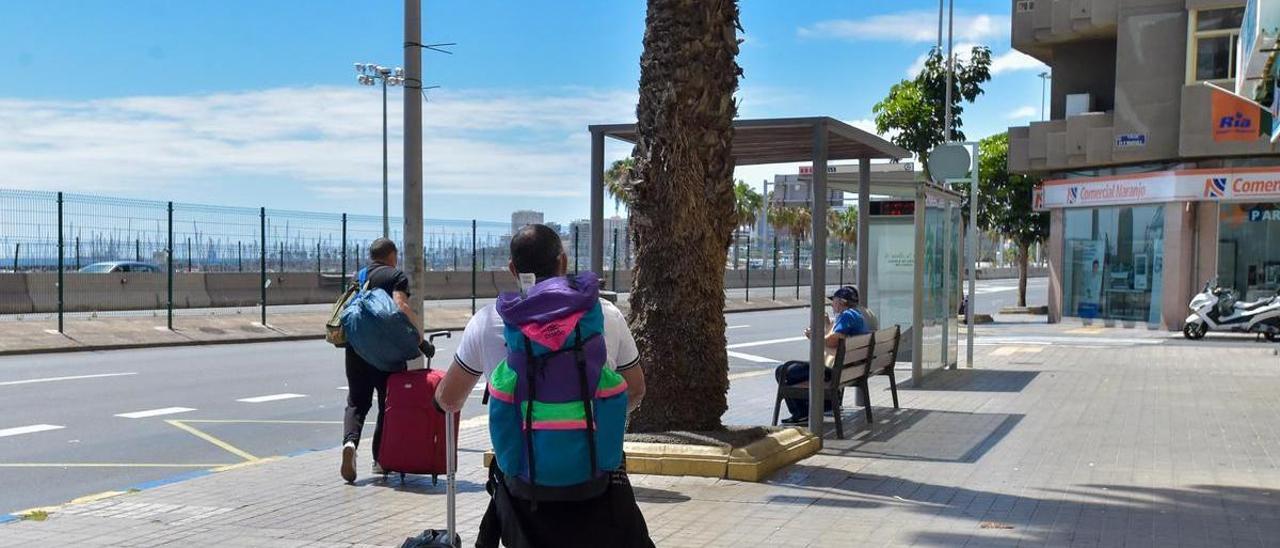 Turistas con maletas en una parada de guaguas.