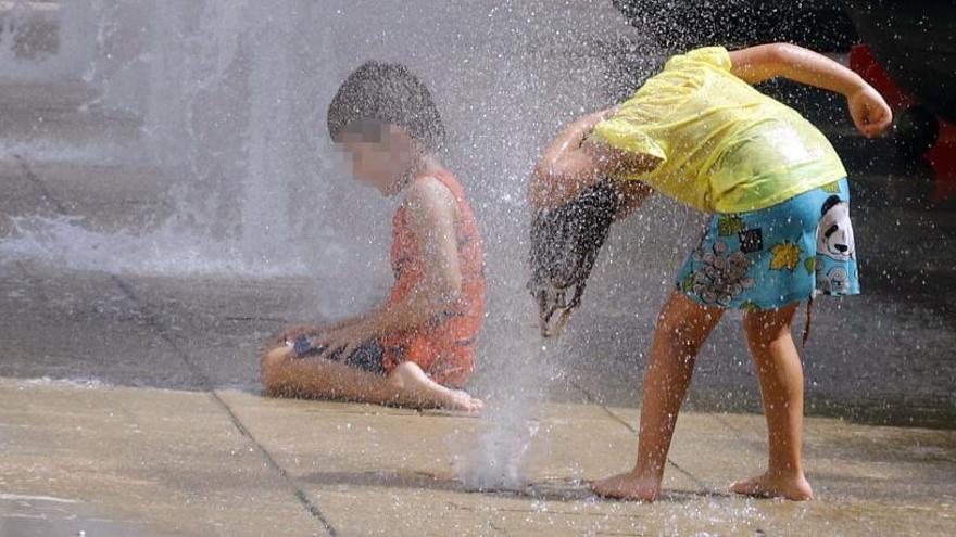 Dos niños juegan en una fuente en un día de calor.