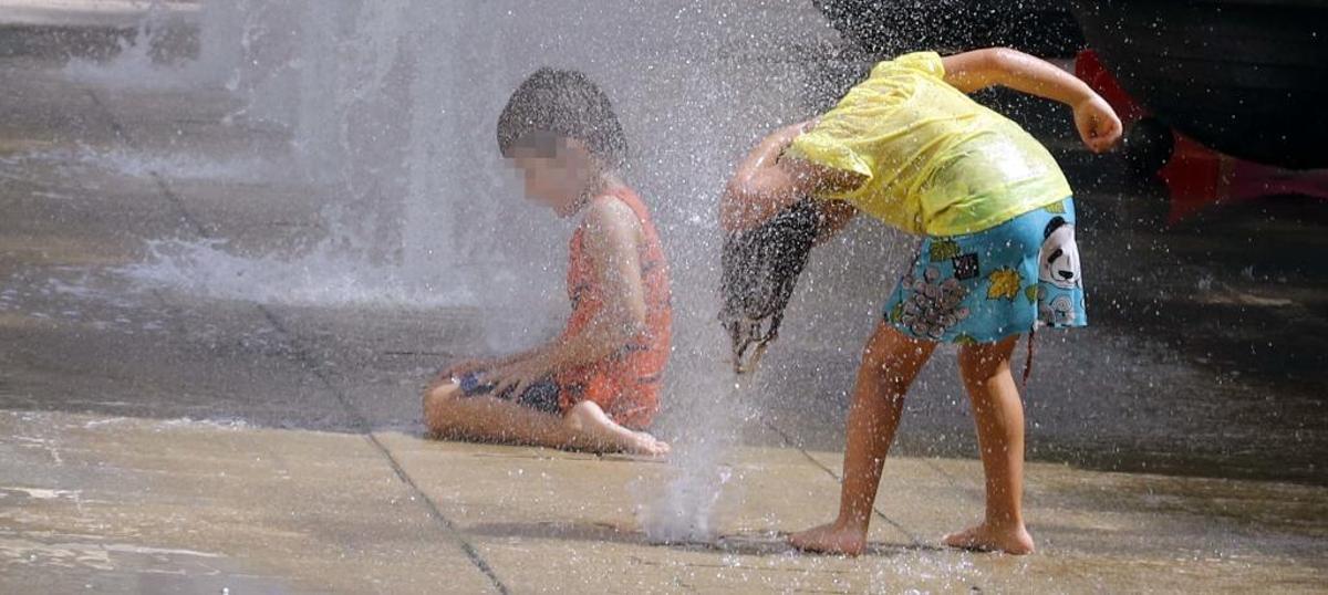 Dos niños juegan en una fuente en un día de calor.