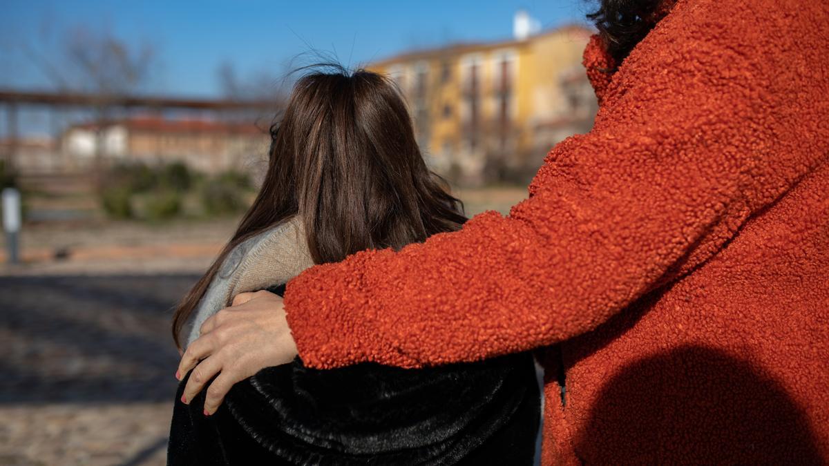 Una persona abrazando a una mujer sentada