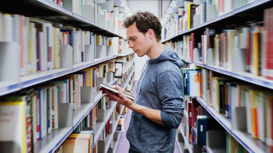 Un estudiante universitario hojea un libro en una biblioteca