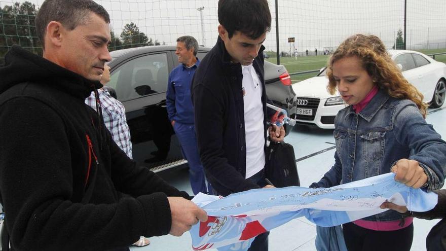 El capitán celeste, Borja Oubiña, firma una bandera con los colores del Celta a          una joven aficionada al término del entrenamiento celebrado ayer a puerta cerrada en A Madroa. // Jorge Santomé