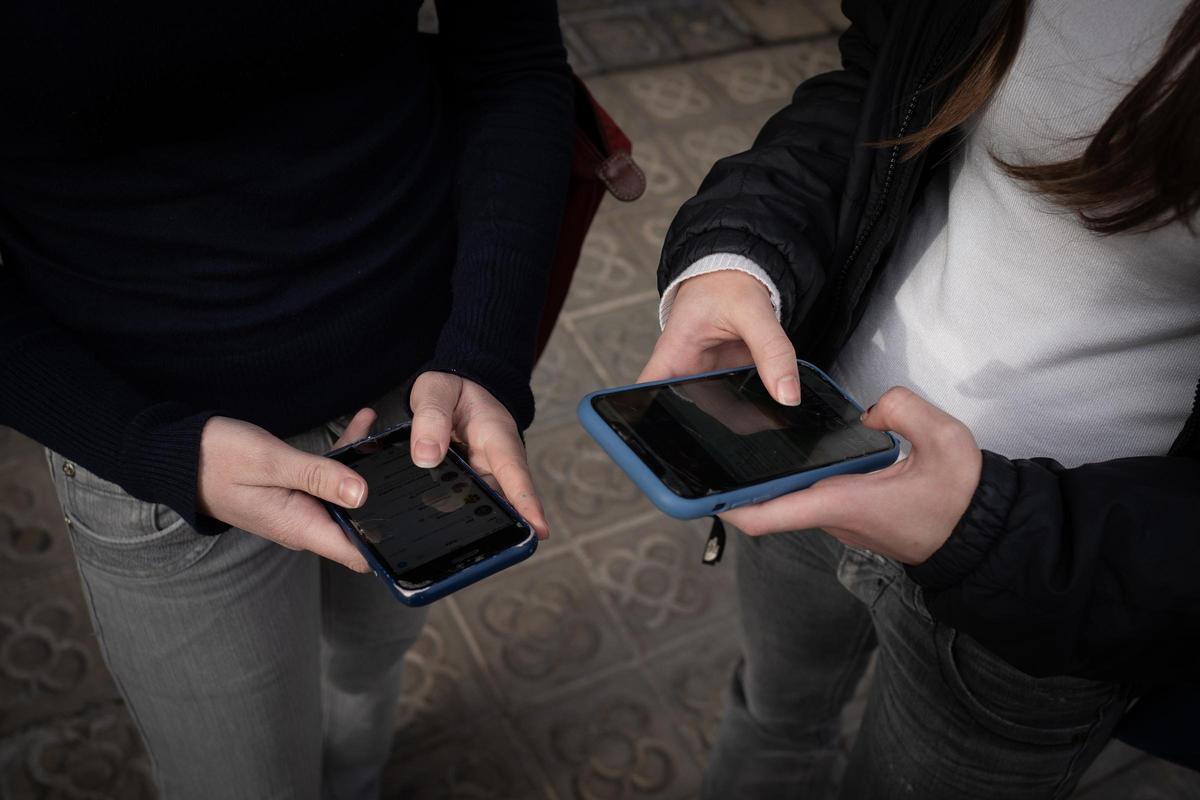 Dos jóvenes consultan su teléfono móvil