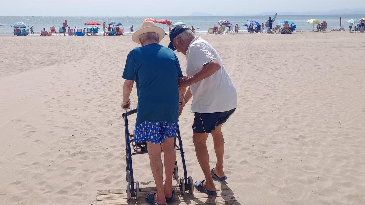 Un veraneante con andador intenta descender de la pasarela al arenal.