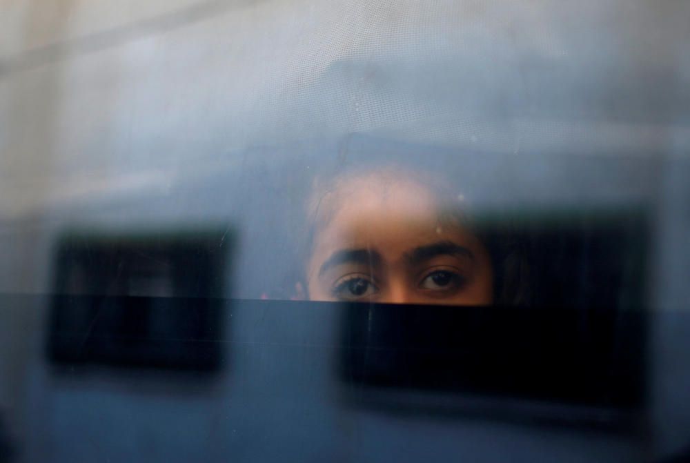 Palestinian girl looks out a bus window as she ...