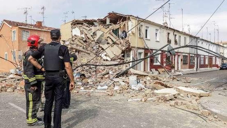 Un agente y varios bomberos ante la casa derrumbada.