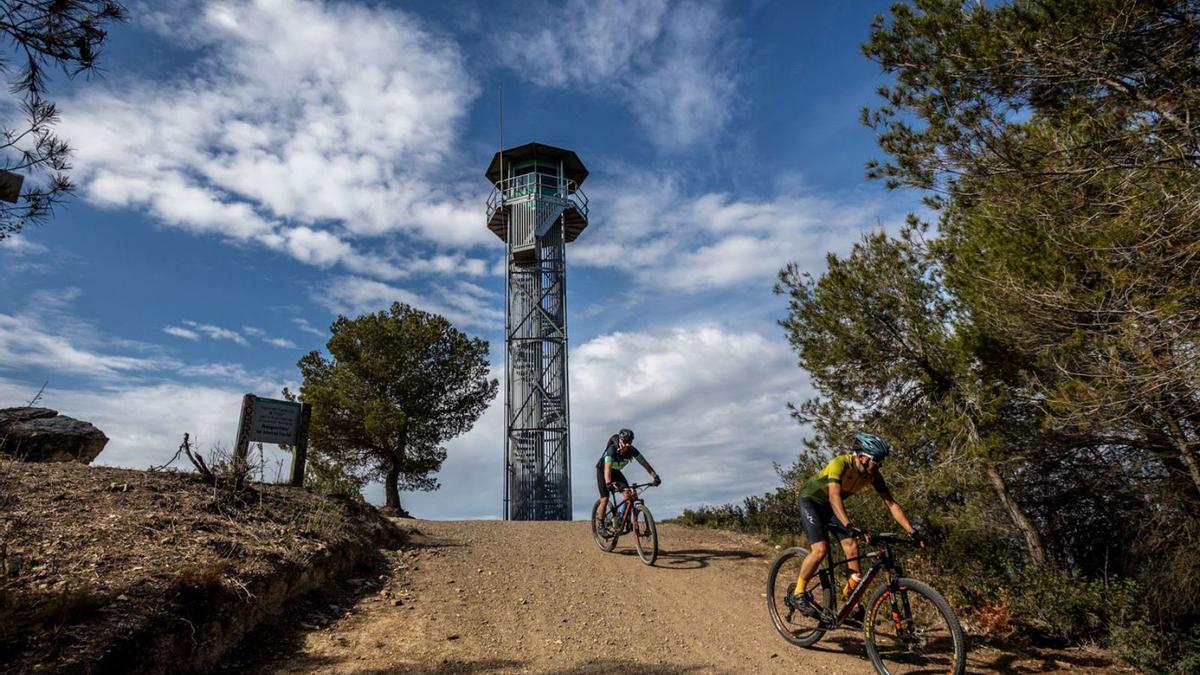 Un par de ciclistas pedalean junto a una de las torres de vigilancia de Collserola