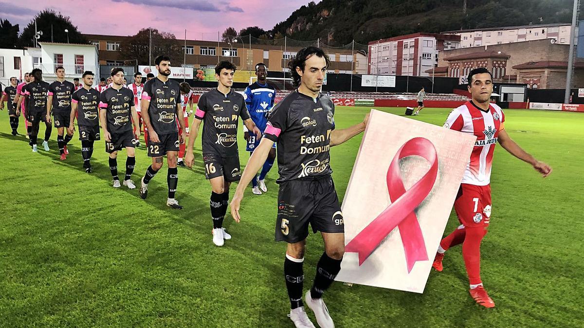 Los jugadores salen al terreno de juego portando un gran lazo que refleja la lucha contra el cáncer de mama, ayer. | CD Laredo