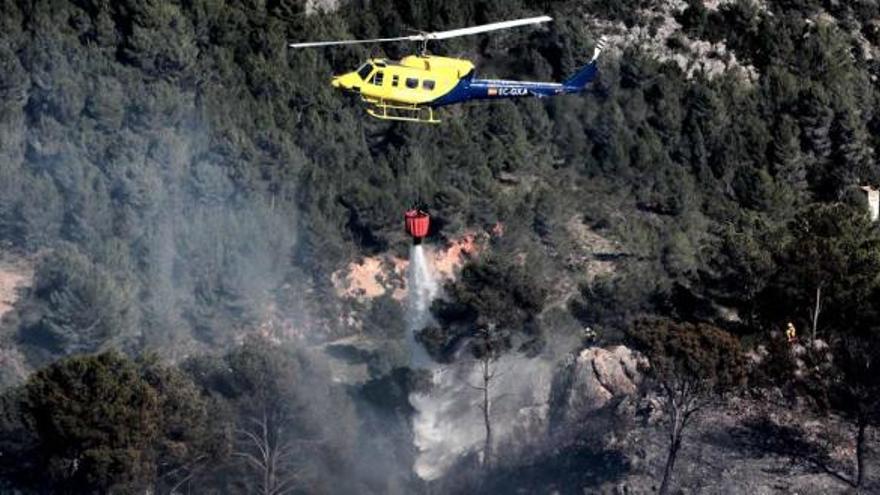 Uno de los helicópteros que participó en las labores de extinción lanza agua sobre la zona afectada, un terreno muy abrupto que dificultó el acceso por tierra.