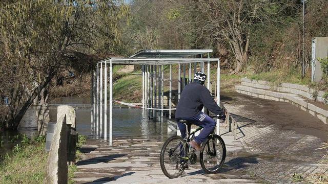 Un ciclista observa el manantial mineromedicinal de O Tinteiro, engullido por las aguas del río.