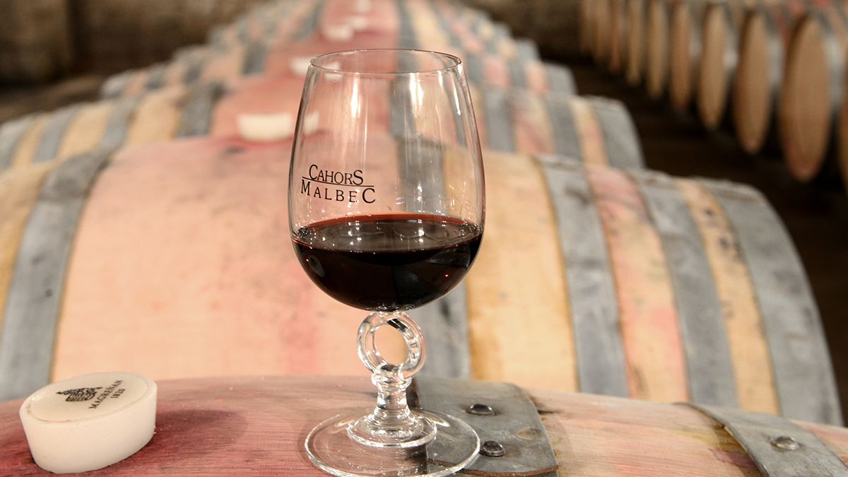 Una copa de malbec de Cahors, el célebre “vino negro” del Lot, reposando entre barricas en una bodega tradicional