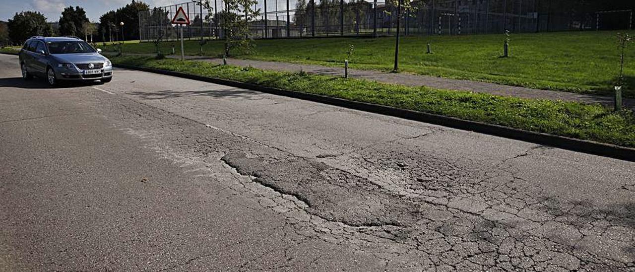 Un vehículo circula por uno de los viales del campus universitario, lleno de desperfectos, con el aulario a la derecha. | Ángel González