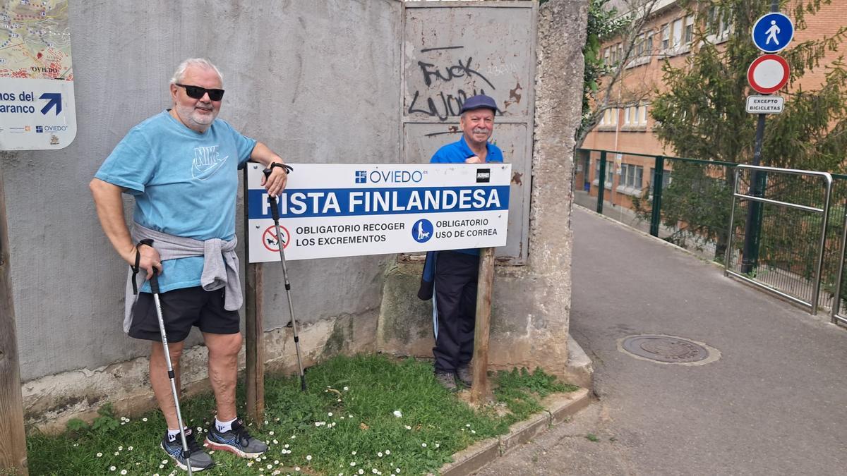 José Manuel Bravo y Adolfo Secades apoyados en el cartel que marca el inicio de la pista finlandesa en Ciudad Naranco.