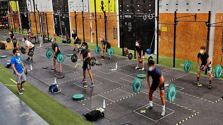 Varias personas entrenan con mascarilla en un centro deportivo.